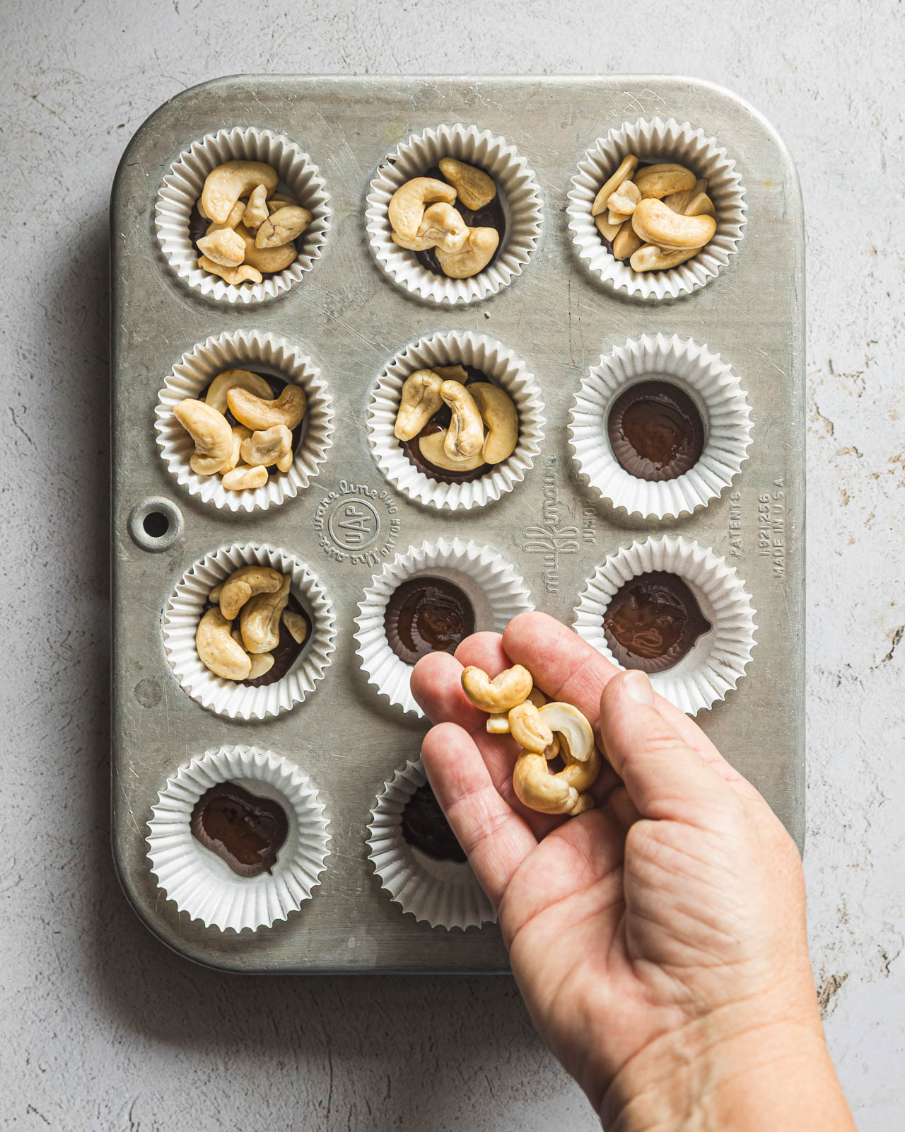 Adding raw cashews to mini muffin liners with melted dark chocolate