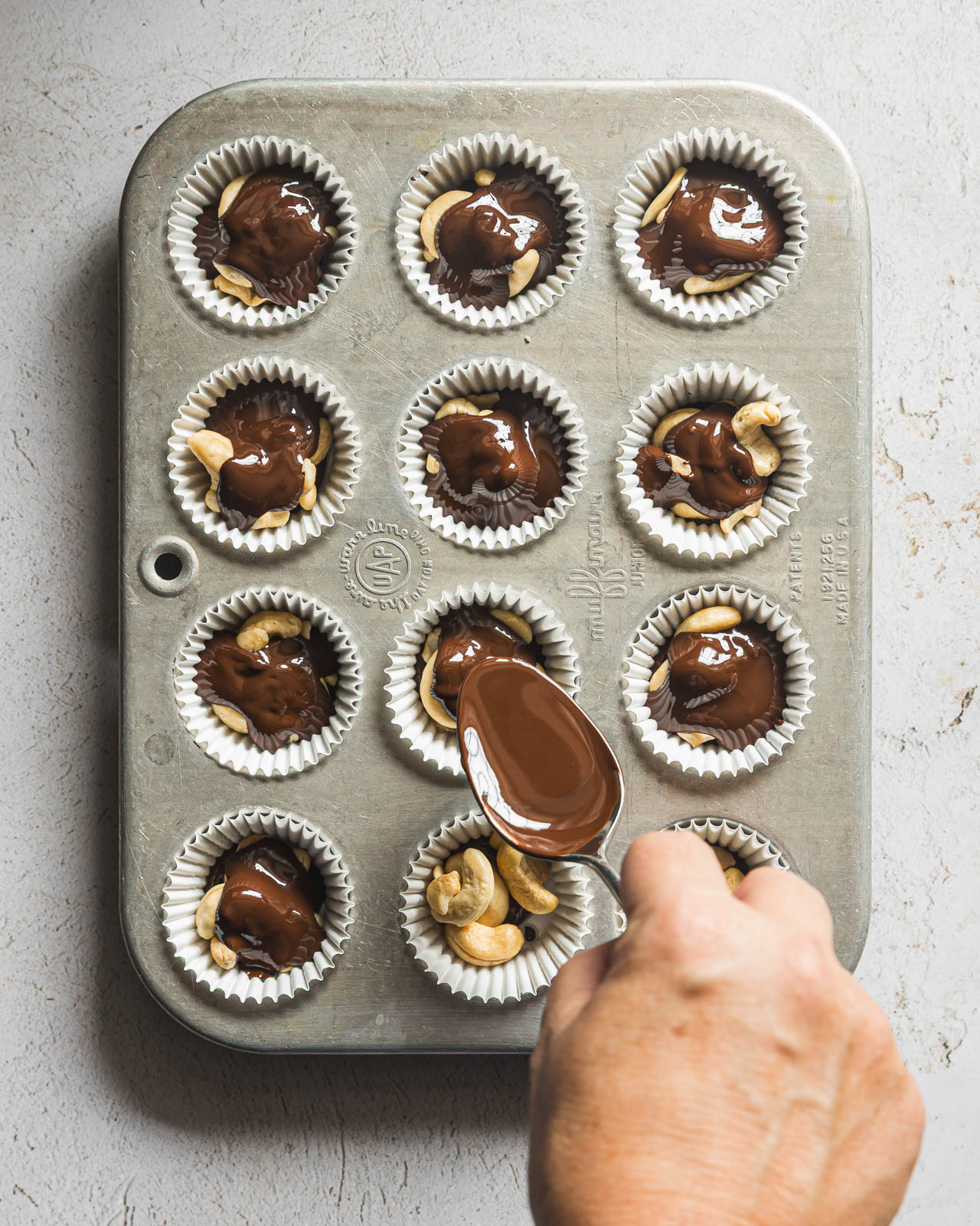 Spooning melted dark chocolate over cashews in mini muffin cups