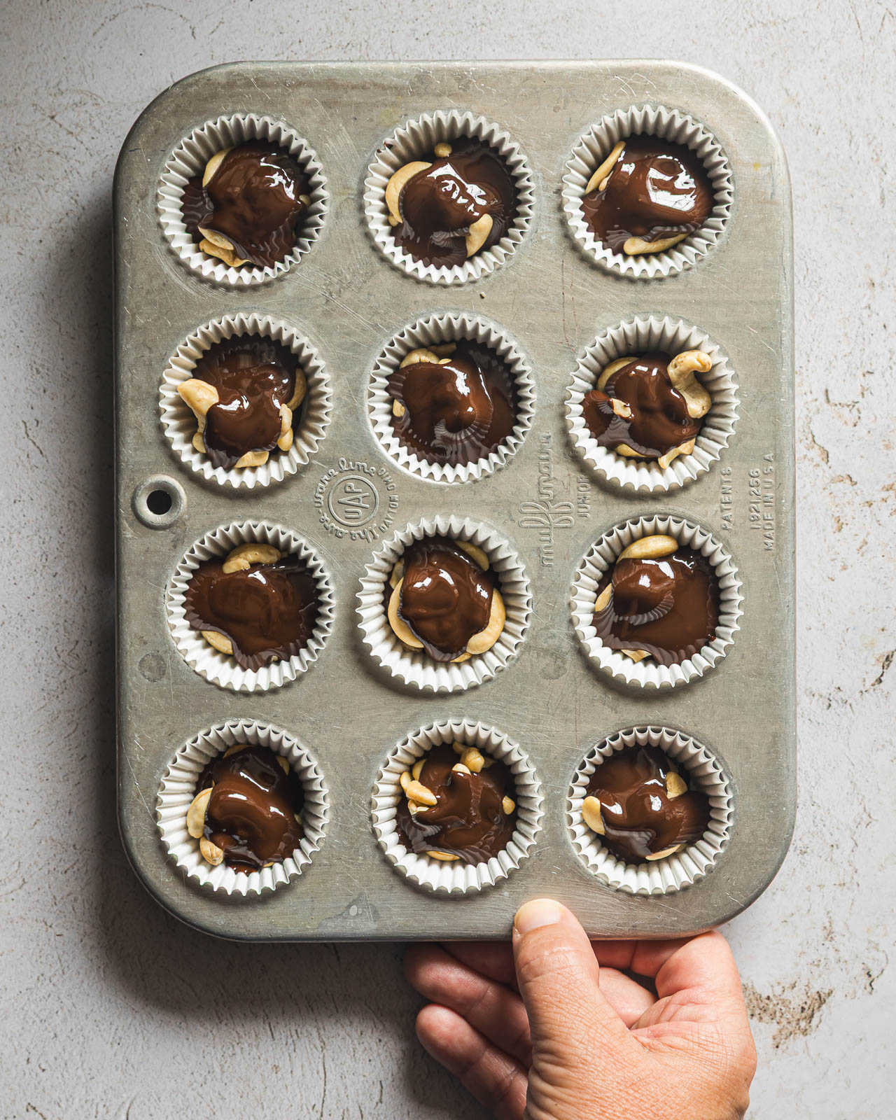 Gently jiggling the mini muffin pan to spread melted chocolate around the cashews