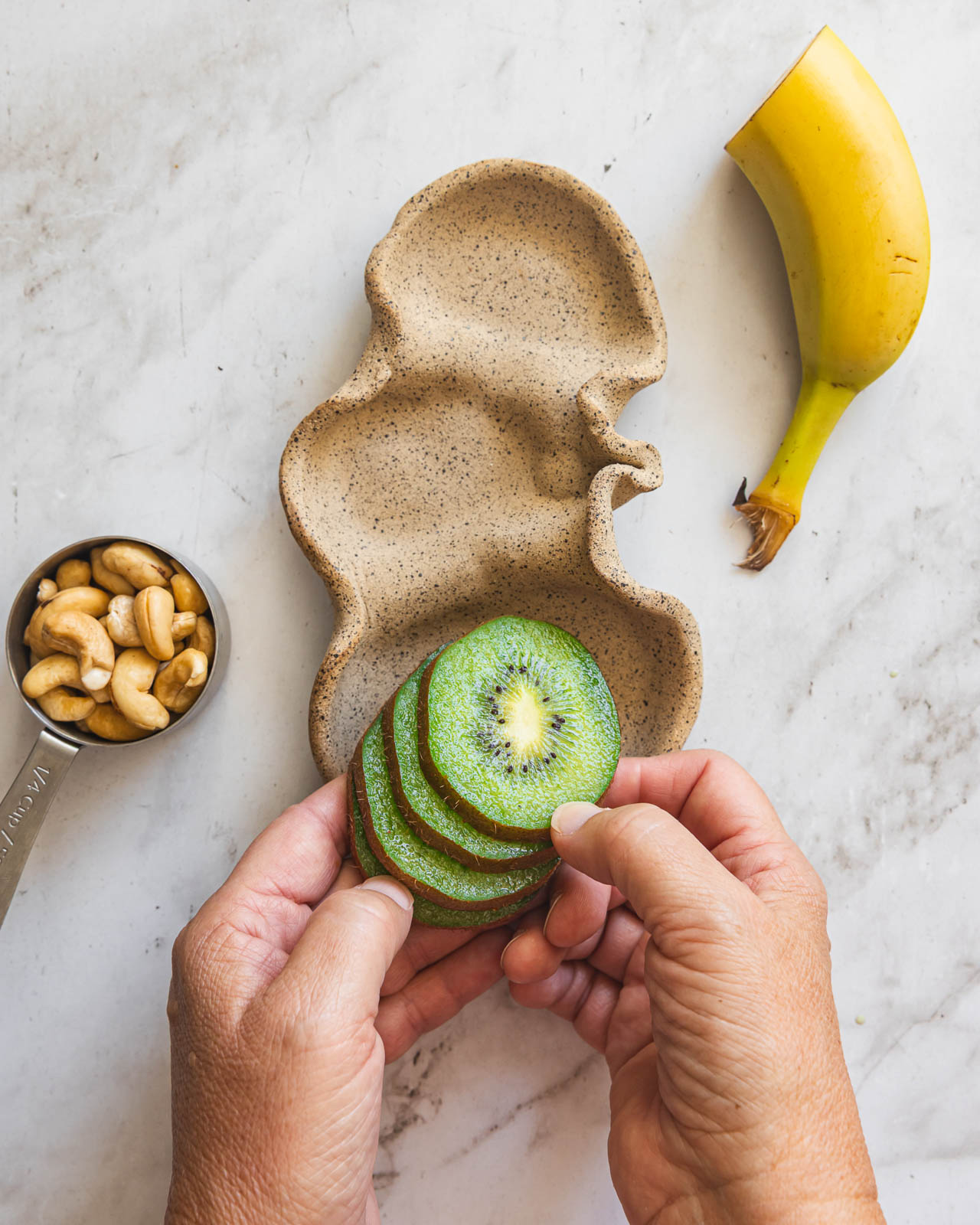 Adding sliced kiwi to a snack plate with cashews