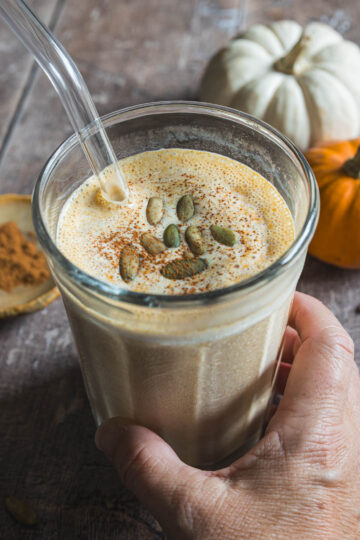 Hand holding a pumpkin smoothie topped with pepitas and pumpkin pie spice