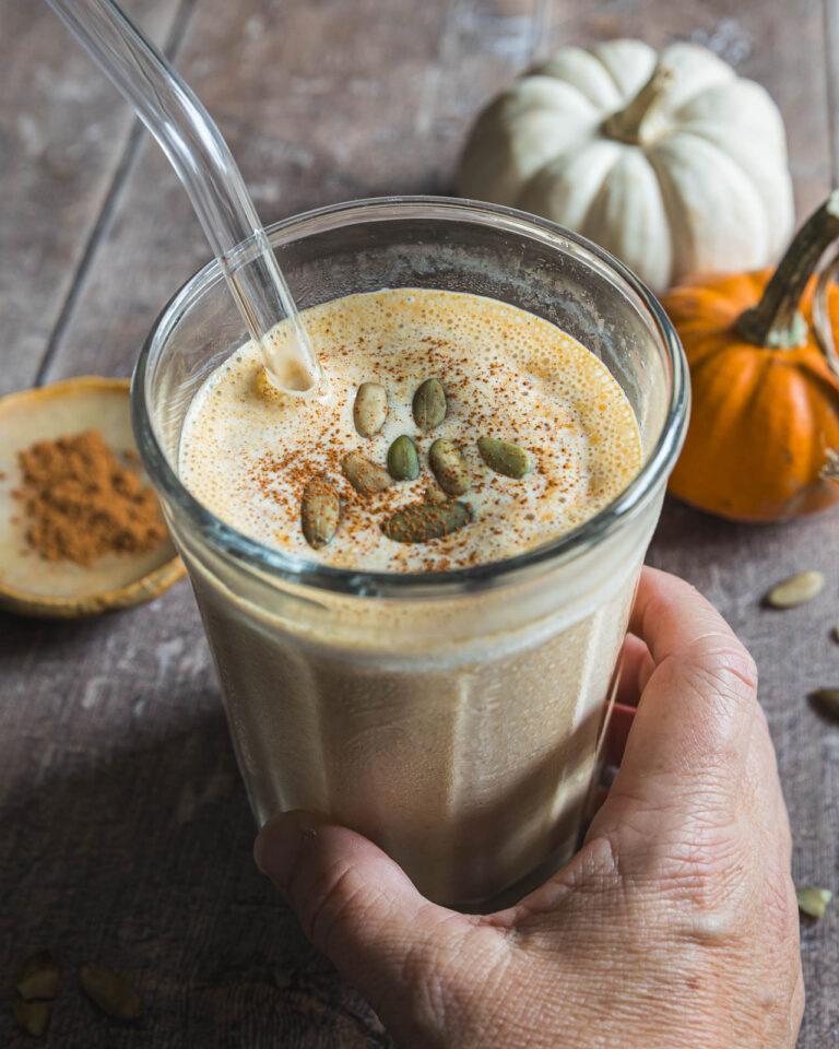 Hand holding a pumpkin smoothie topped with pepitas and pumpkin pie spice
