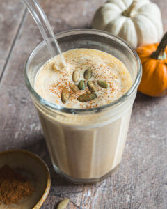 Pumpkin smoothie topped with pepitas and pumpkin pie spice with small pumpkins in the background