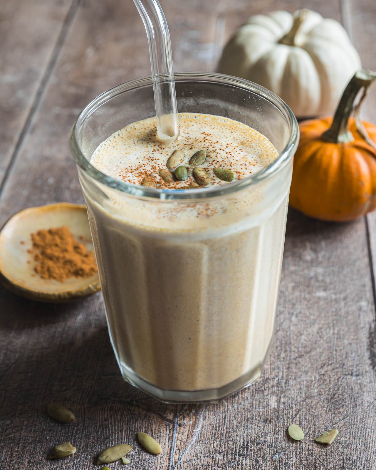 Glass of creamy pumpkin smoothie garnished with pepitas and pumpkin pie spice