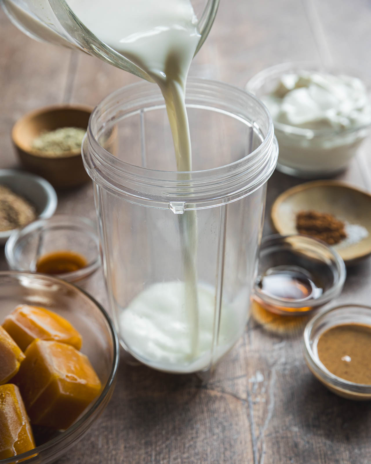 Milk being poured into a blender cup surrounded by ingredients for a pumpkin smoothie