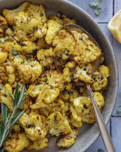 Close-up of roasted cauliflower with Parmesan, toasted pine nuts and fresh herbs in a serving bowl