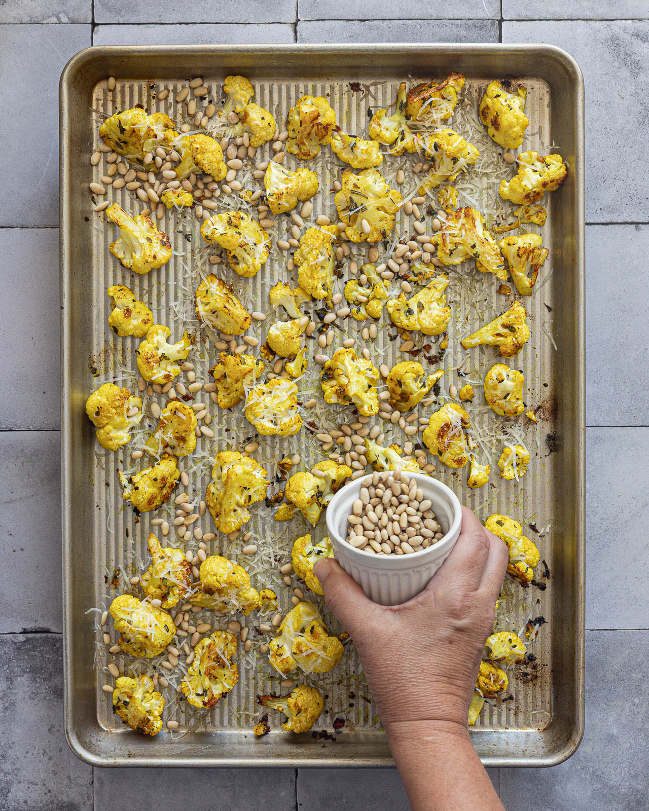 Pine nuts and Parmesan being added to roasted cauliflower on a sheet pan