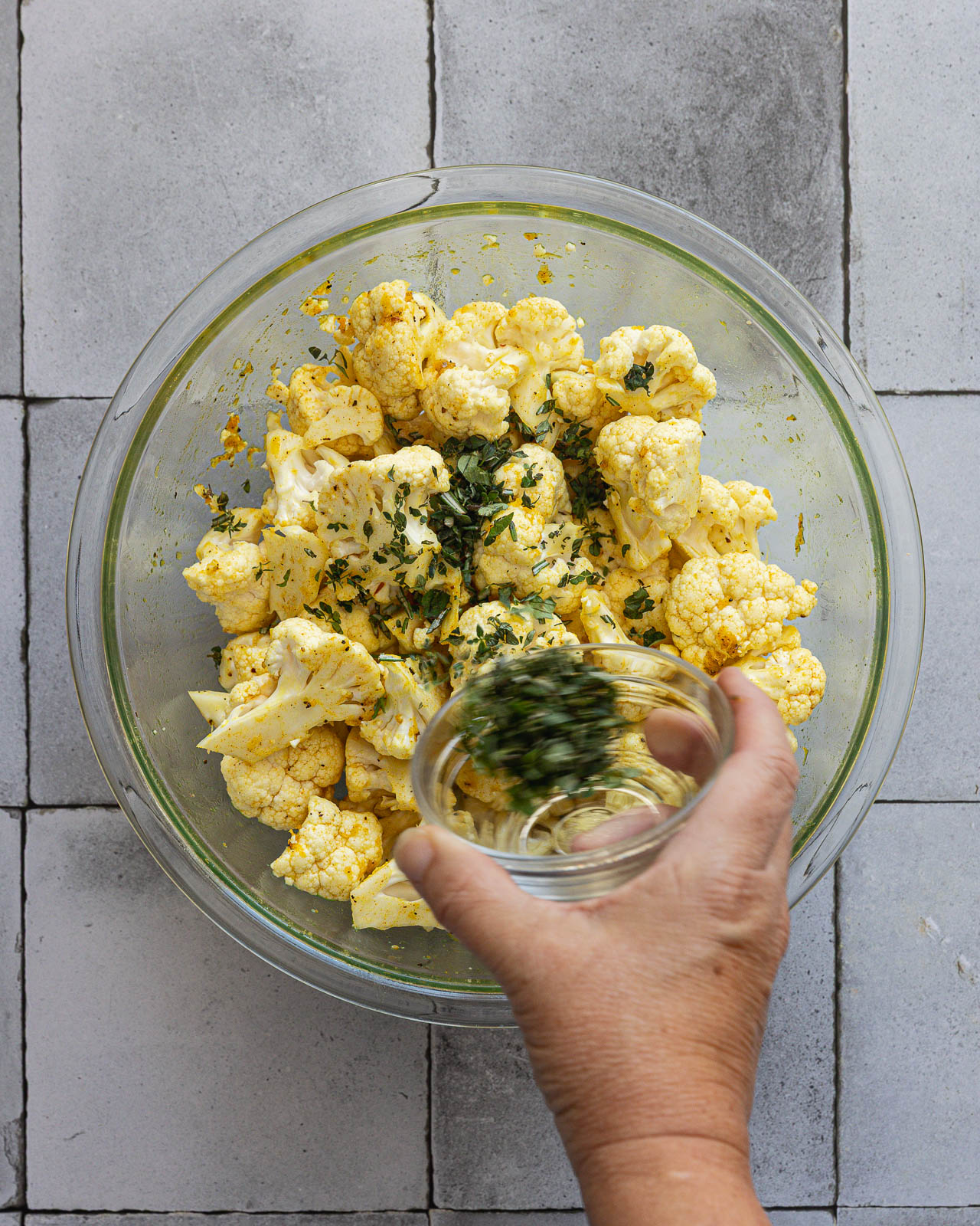 Fresh rosemary, thyme and oregano being added to seasoned cauliflower florets