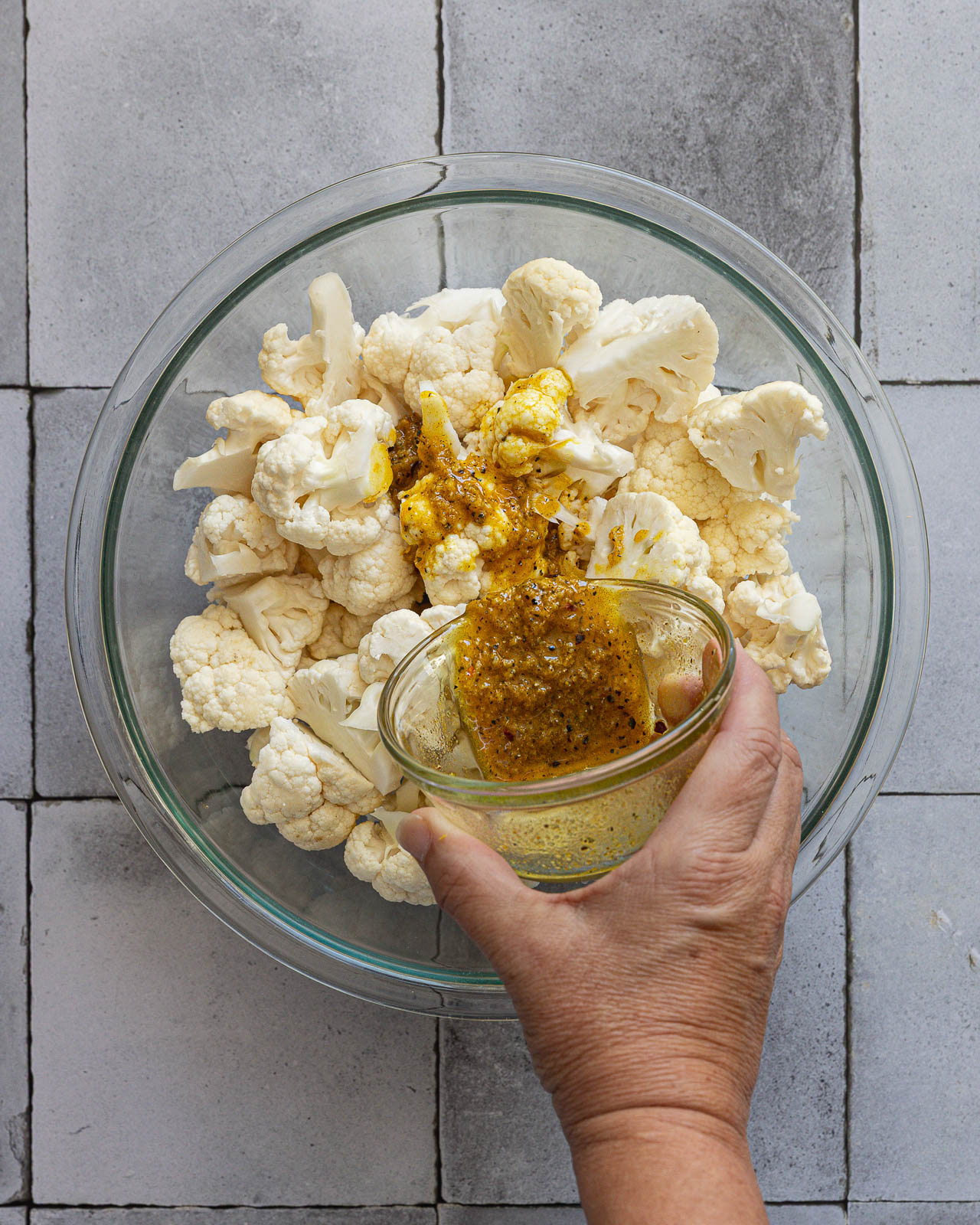 Garlic, lemon zest and turmeric olive oil being poured over cauliflower florets