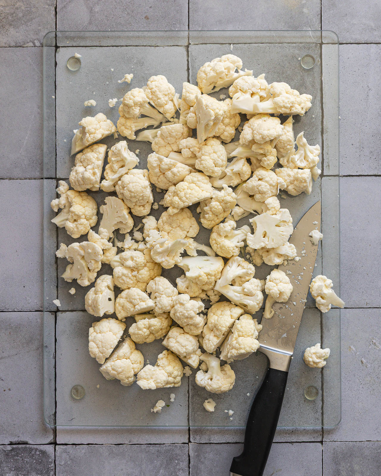 Bite-size cauliflower florets on a cutting board beside a kitchen knife