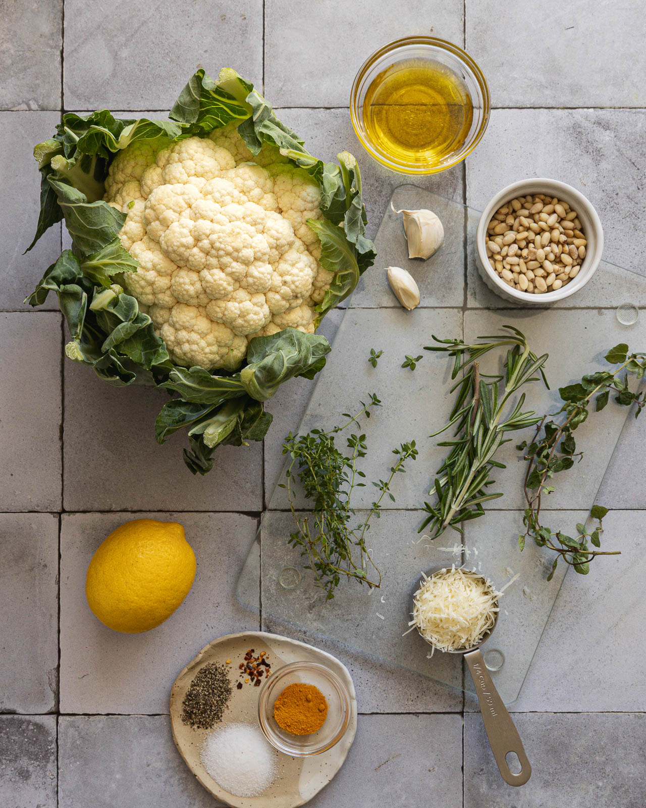 Cauliflower, Parmesan, pine nuts, turmeric, lemon, olive oil and fresh herbs arranged on a table