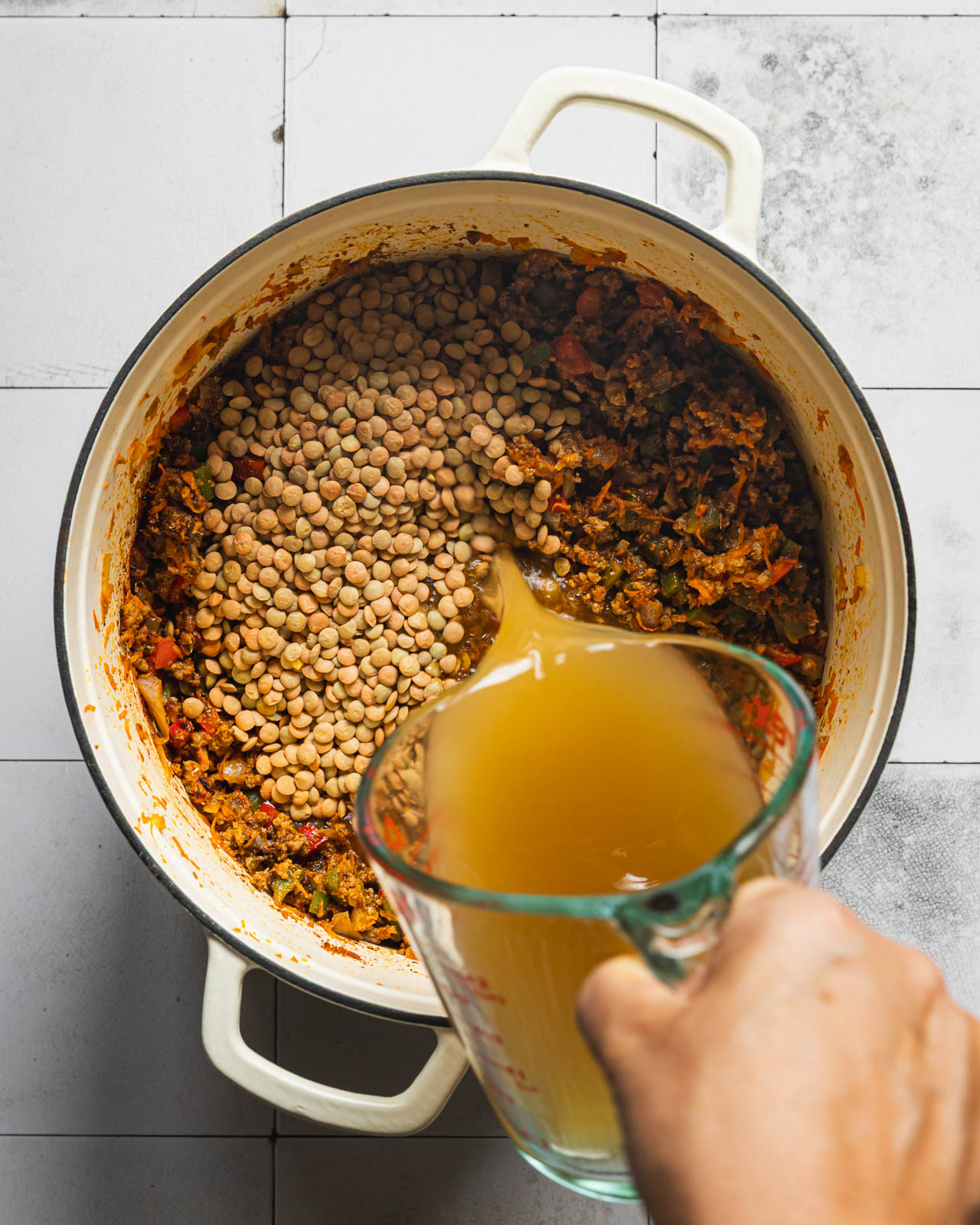 Pouring broth over brown lentils and ground beef in a Dutch oven