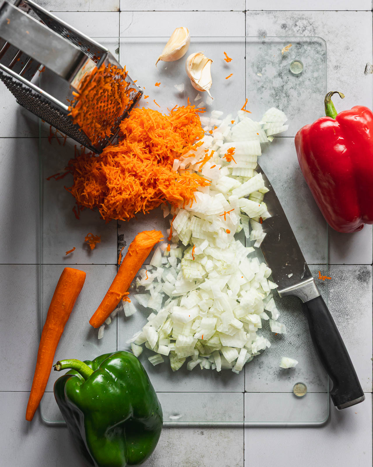 Finely grating carrots beside chopped onion and bell peppers