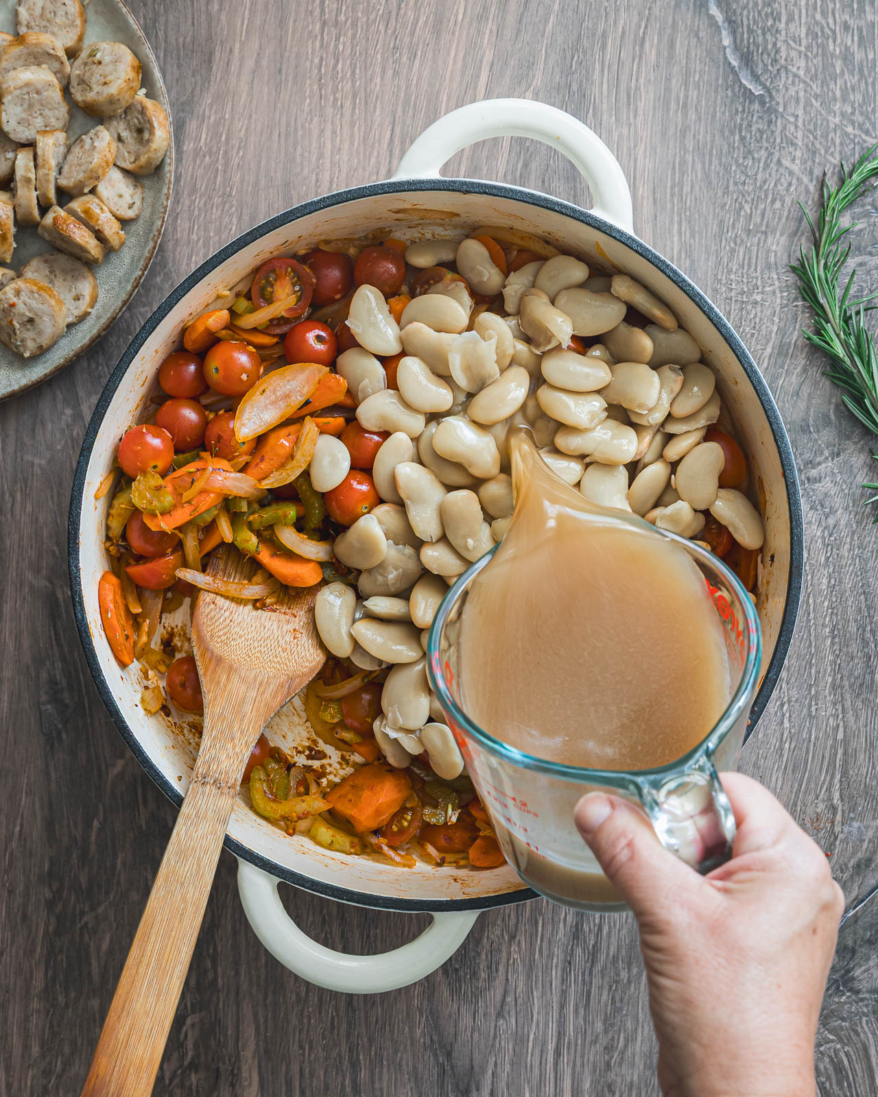 Chicken broth being poured over butter beans and vegetables in a braiser