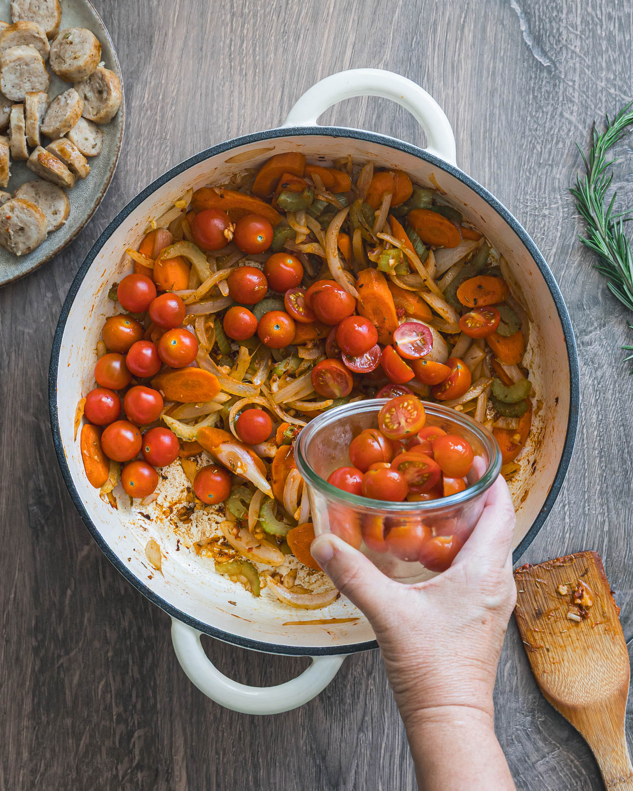 Grape tomatoes being added to sautéed onions, carrots and celery