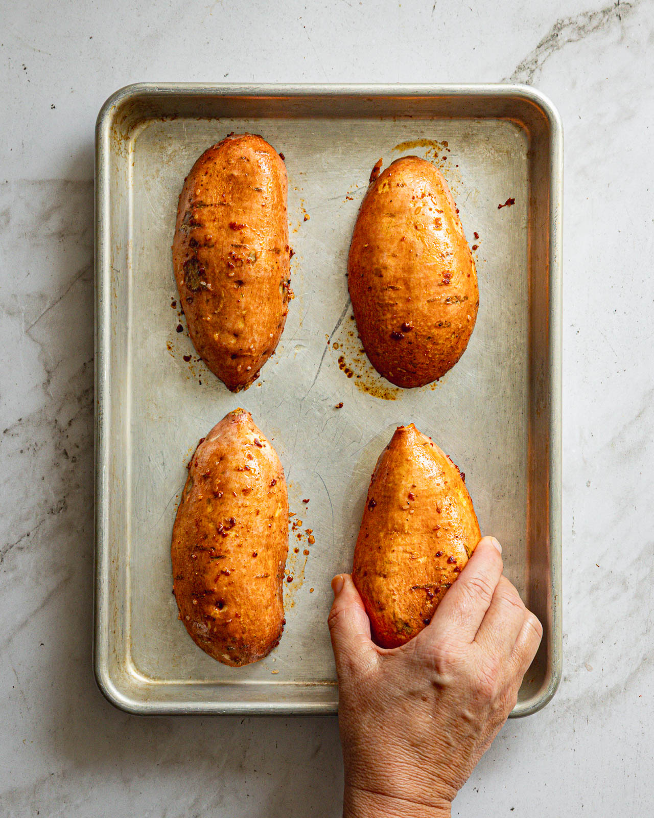 Seasoned sweet potato halves placed cut-side down on an aluminum sheet pan