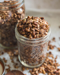 Chocolate granola with cacao, nuts and seeds overflowing from a glass mason jar