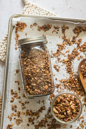 Homemade chocolate granola in a mason jar and small bowl with granola scattered around them
