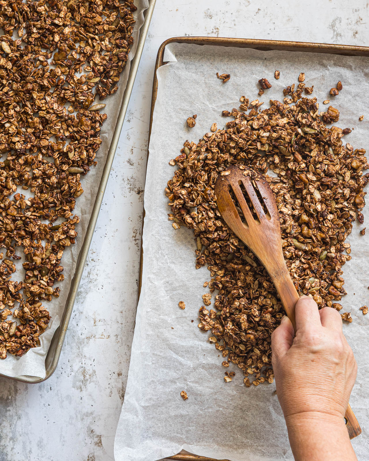 Chocolate granola being stirred on a parchment-lined baking sheet